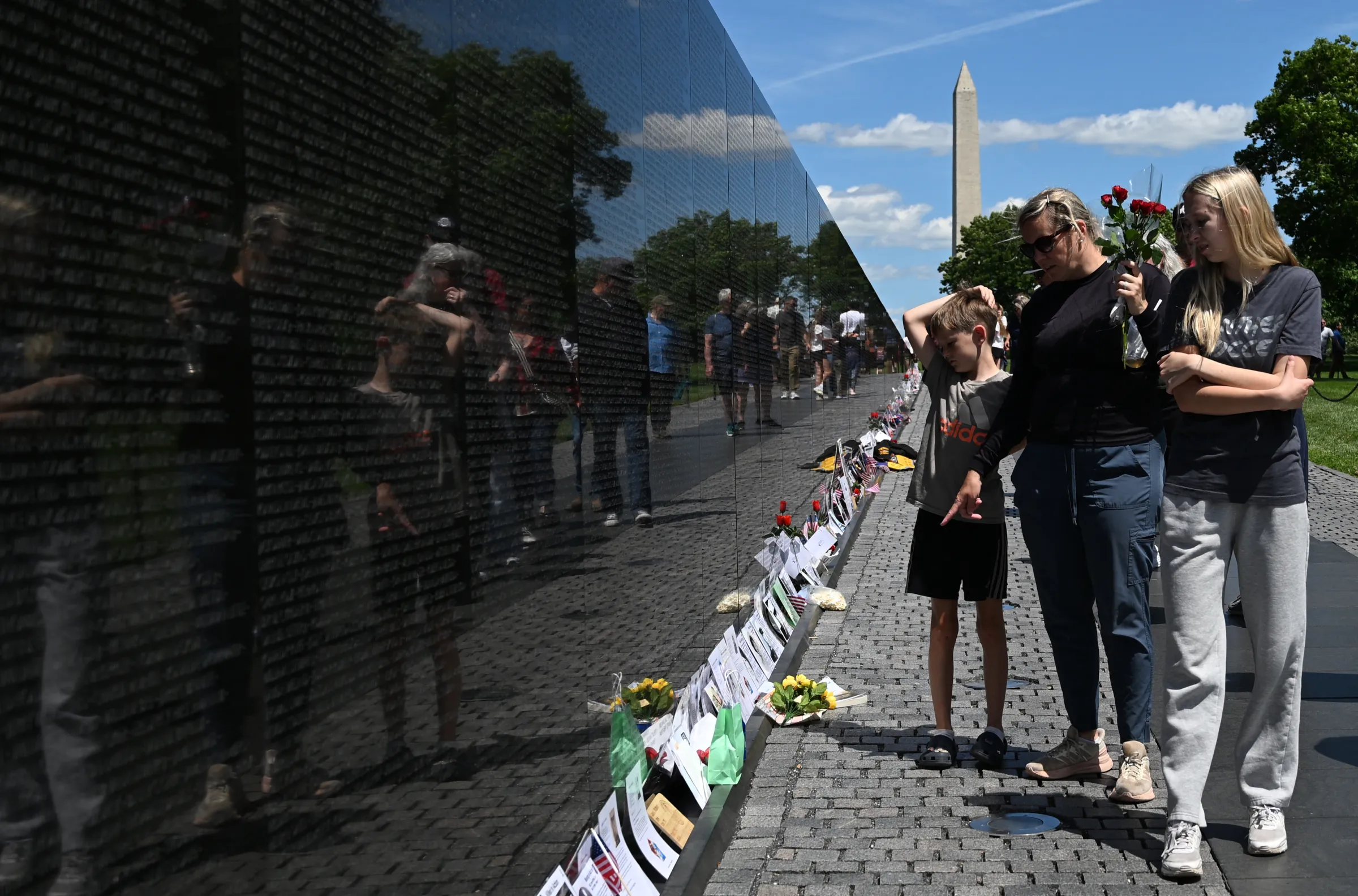 People stand and look at the long black wall of the Vietnam Veterans Memorial.