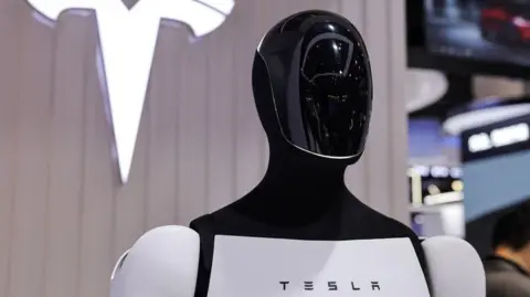 Reuters A Tesla Optimus robot next to a logo at the company’s booth at the 8th China International Import Expo in Shanghai, China
