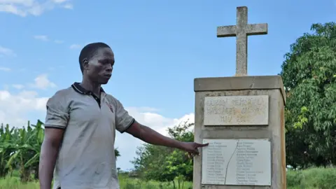 Muhammad Olanya pointing at a memorial for those who died in the village of Lukodi
