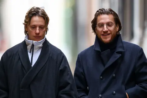 Reuters A blonde man in a big coat walks next to a bearded man wearing glasses