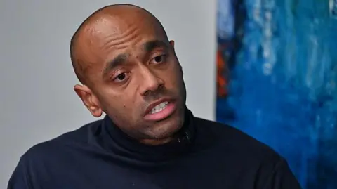 AFP via Getty Images Noureddin Bongo, the son of Gabon's deposed leader Ali Bongo, in a black sweater, takes part in an interview