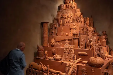 AFP/Getty Images Someone looking at Yinka Shonibare's Monument to the Restitution of the Mind and Soul - a pyramid-shaped unit featuring more than 150 clay replicas of the Benin Bronzes.