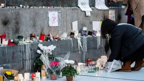 MAGALI COHEN/Hans Lucas/AFP A photograph taken on November 11, 2025 shows candles and flowers displayed at a makeshift memorial in tribute of the victims of Paris attacks of November 13, 2015, on the place de la Republique, in Paris