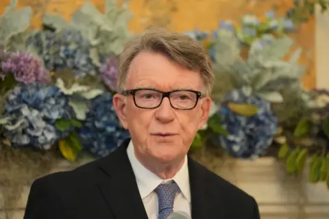 PA Media Peter Mandelson, wearing black framed glasses, a black suit, shite shirt, and blue tie