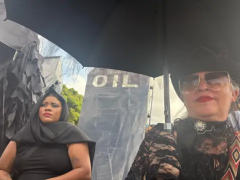 Prostesters in black next to a coffin reading "oil"