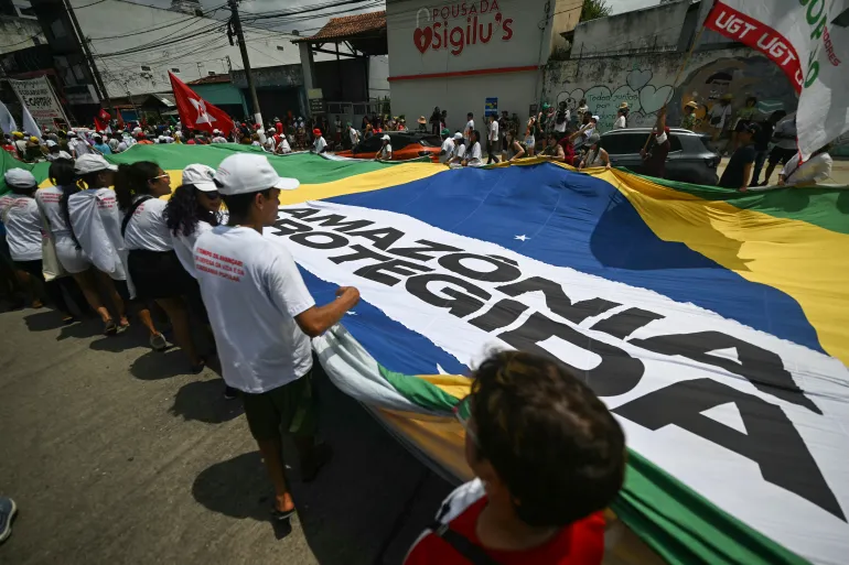 People hold a giant flag reading “Protected Amazon” during the so-called "Great People's March" on the sidelines of the COP30 UN Climate Change Conference in Belem, Para state, Brazil, on November 15, 2025.