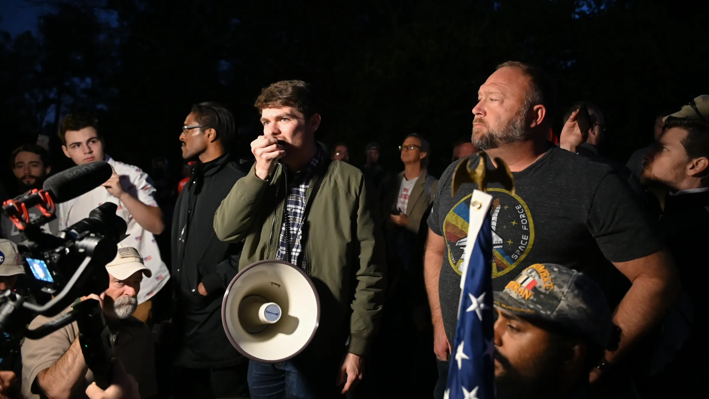 An array of young men stand with cameras, megaphones, and an American flag.