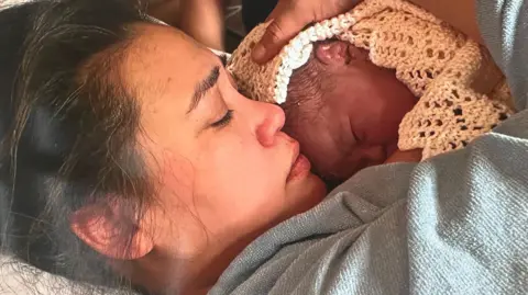 Keira is lying down, cradling her newborn baby Zammi, who's covered in a blanket, into her chest.