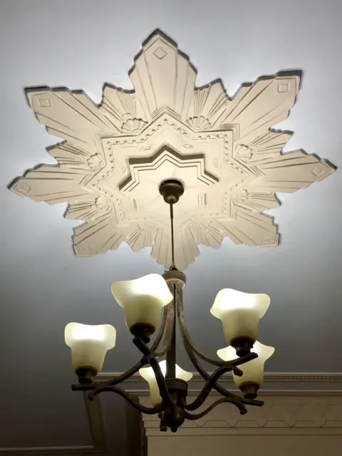 Moorthy’s Furniture Example of Art Deco lighting at the Seksaria building in Marine Drive. The light has five bulbs in a candelabra-style fitting, with a geometric star design on the ceiling around it. 