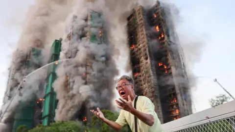Reuters  A man gestures in distress as the tower blocks burn behind him.