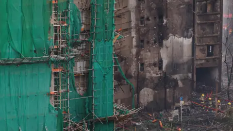 Reuters Firefighters walk past charred bamboo scaffolding at Wang Fuk Court after a fire 