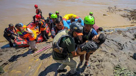 AFP via Getty Images Rescuers carry a man from a dinghy beached on a muddy bank.
