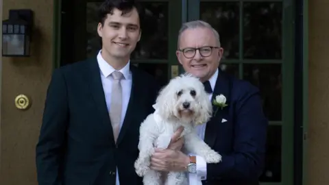 Reuters Australian Prime Minister Anthony Albanese stands with his son Nathan and his dog, ringbearer Toto - they all face towards the camera