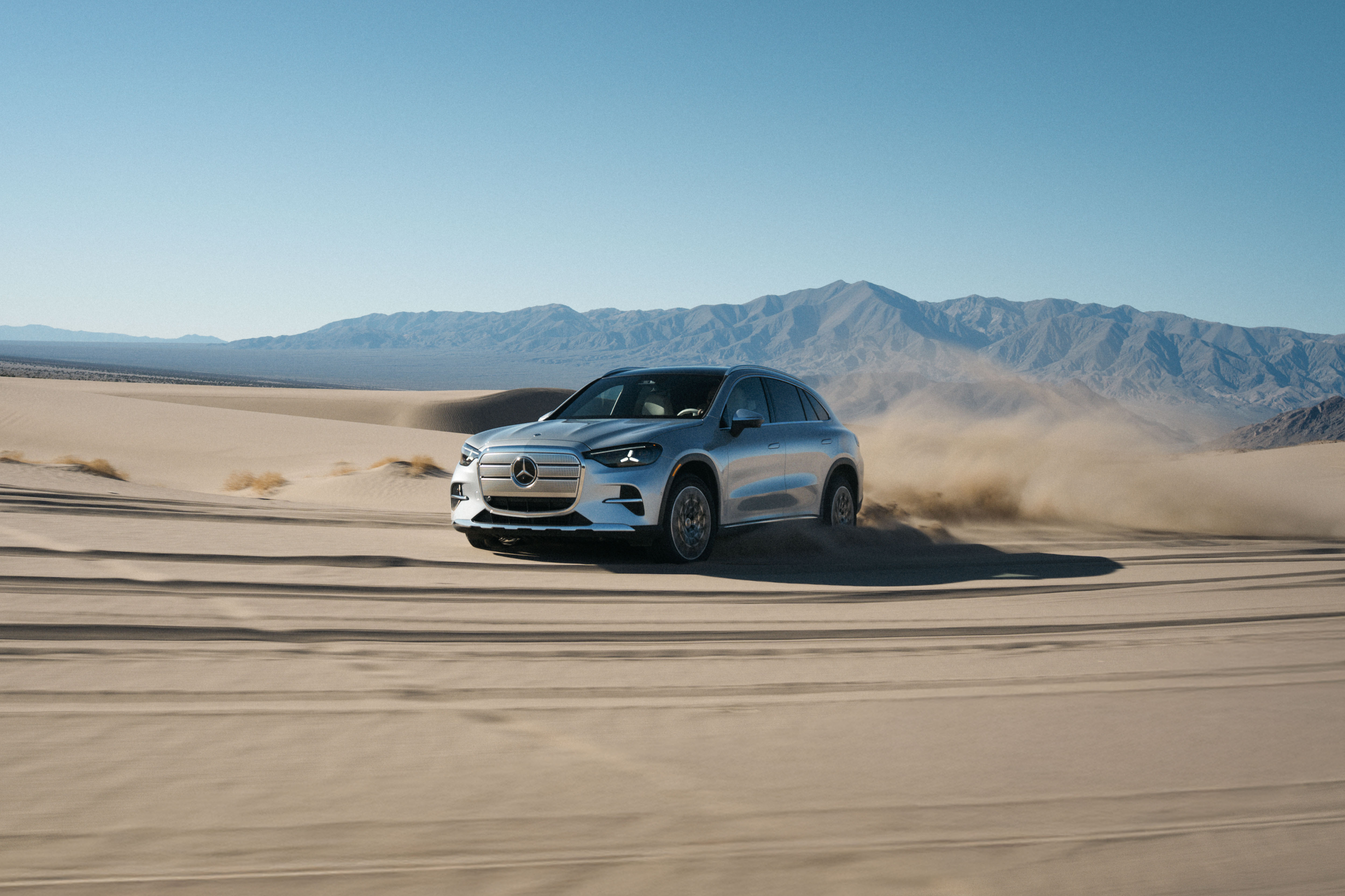 A silver Mercedes GLC drives on a sand dune