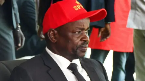 Reuters Benjamin Bol Mel, in black suit and tie, white shirt and red cap written SPLM, attends an SPLM event in Juba, South Sudan
