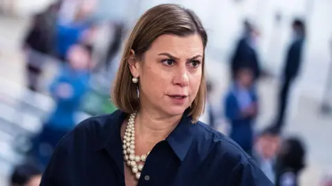Getty Images Elissa Slotkin with medium-length brown hair, a blue shirt and three strings of oversized pearls, looks down and her to her left 