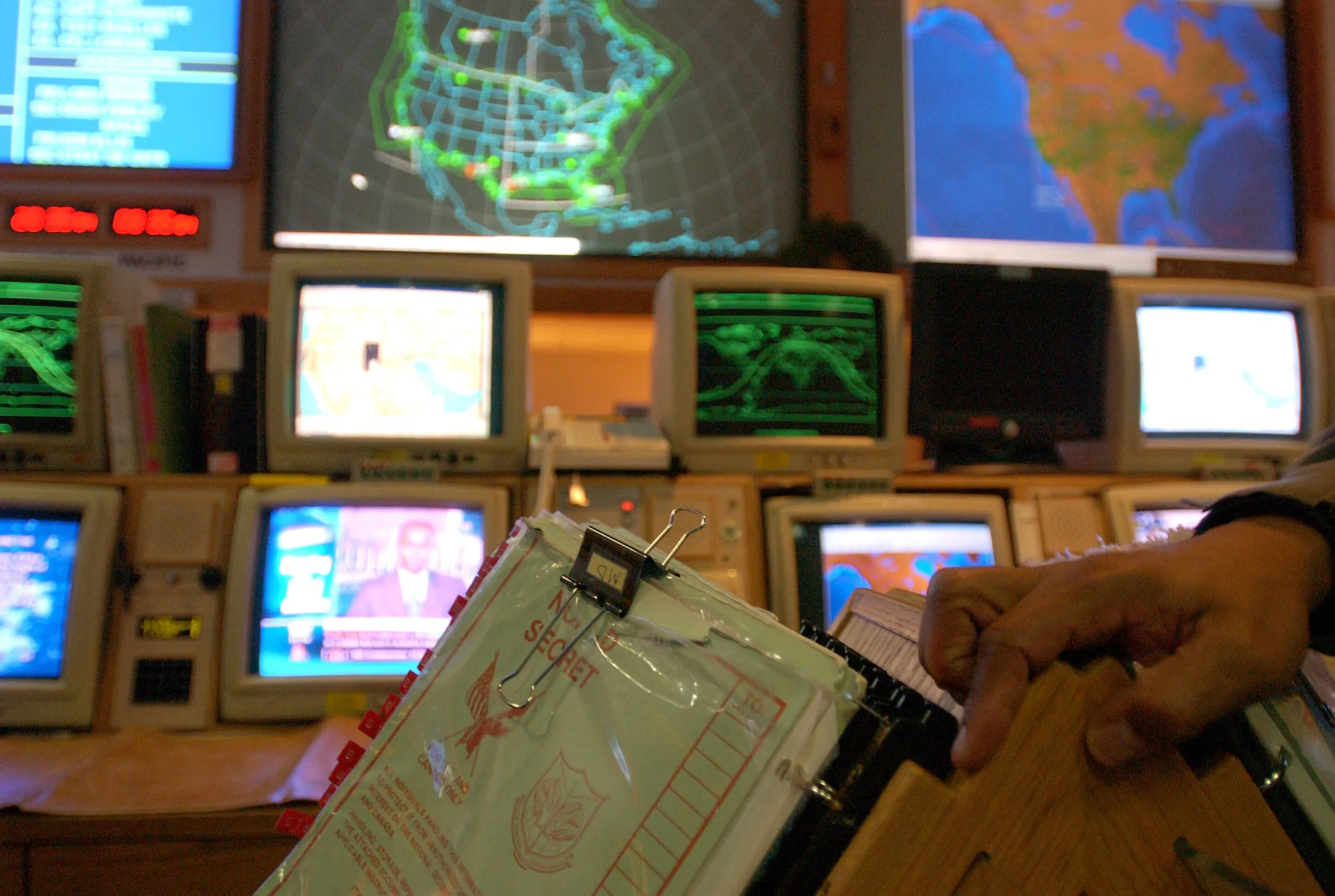 A bank of antiquated computer monitors shows broadcasts, maps and other data.