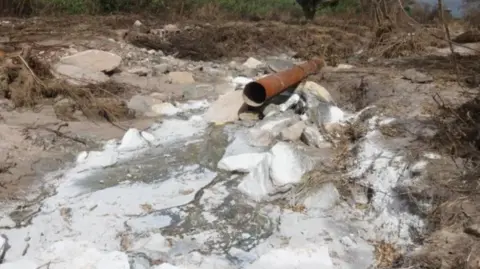 Chongo Sampa / News Diggers A pipe leading to a dry river. The rocks are covered in a white sediment
