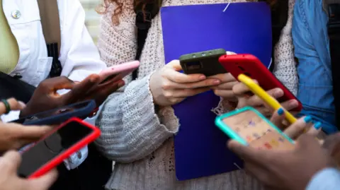 Getty Images A circle of young people from the shoulders down holding a smartphones in multicoloured cases