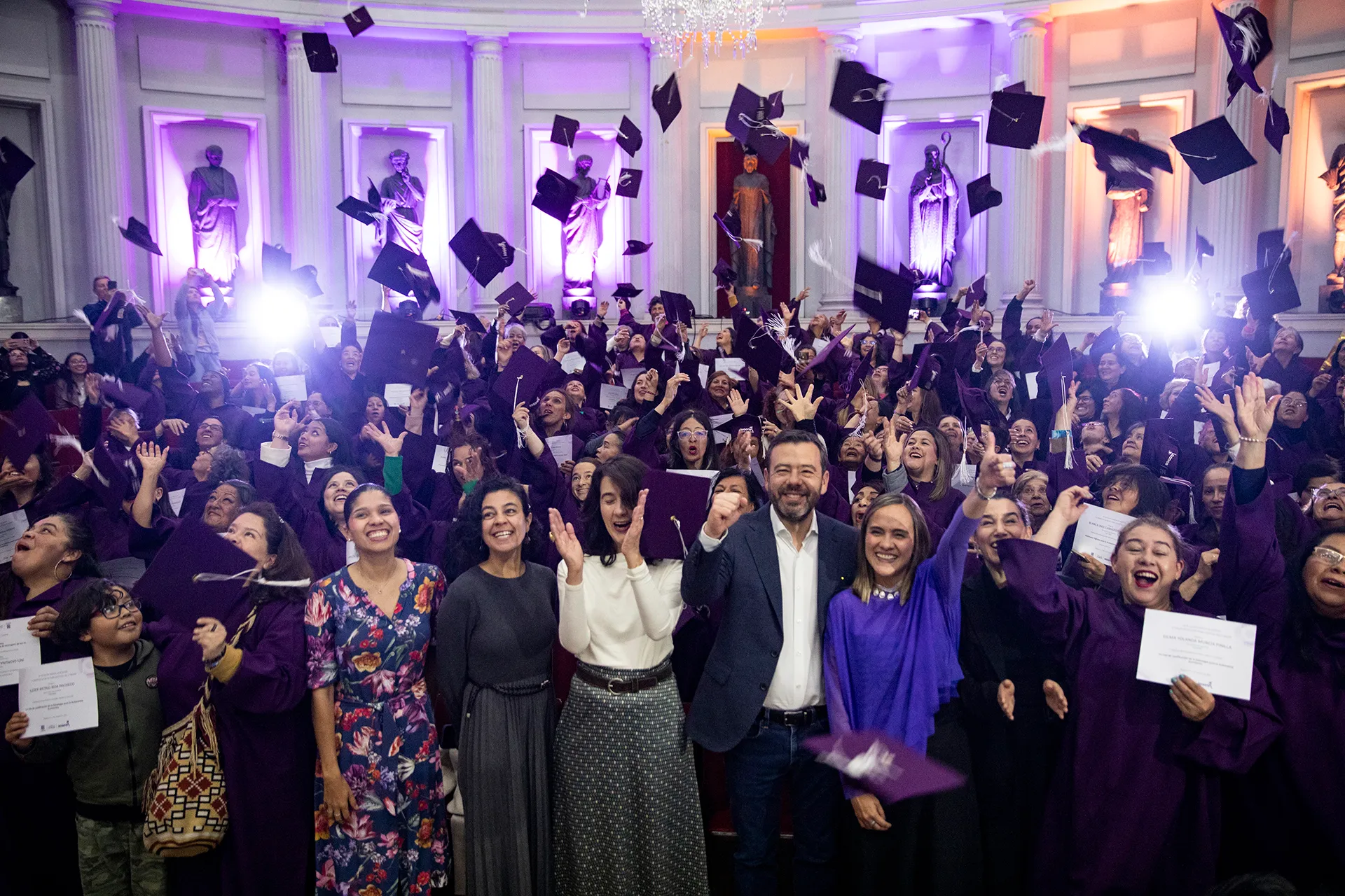 a room filled with people in graduation gowns throwing their caps in the air and cheering