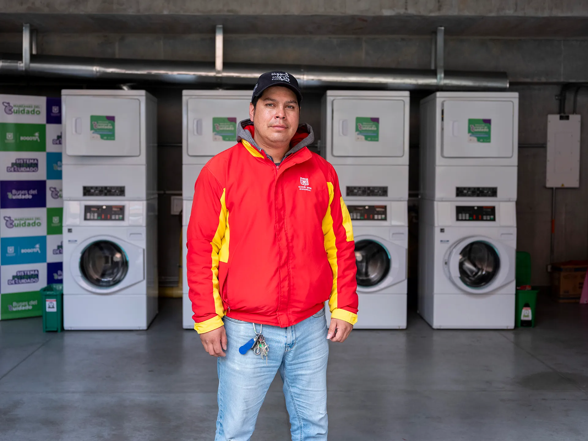 a man wearing jeans and a bright red jacket stands in front of a row of washing machines