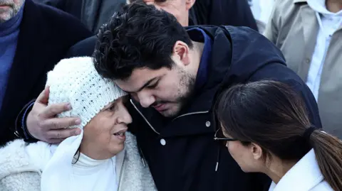 AFP via Getty Images French anti-drug activist Amine Kessaci (C) and his mother Ouassila Benhamdi Kessaci (L) gather to take part in a march in tribute to Mehdi Kessaci at the roundabout where he was murdered and to protest against drug trafficking, in Marseille, southern France on November 22, 2025. 