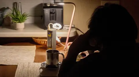 Shutterstock A local woman speaks by phone with a reading lamp connected to a power bank, during a blackout.