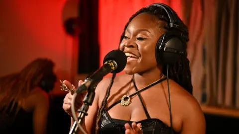 Sampa the Great sings into a microphone, wearing headphones.