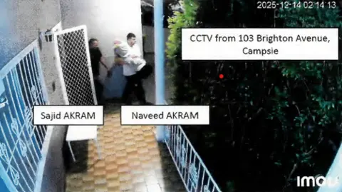 Supplied Grainy footage shows two men coming out of a doorway carrying big unidentifiable objects in their arms.