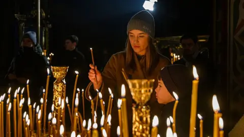 Getty Images A woman lights a candle with her son during an Christmas Eve service in Kyiv, Ukraine on 24 December 2025.