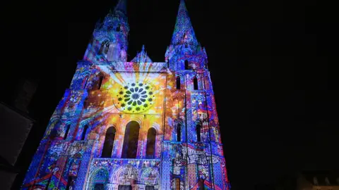 Getty Images The Notre-Dame Cathedral is illuminated in bright colours ahead of midnight Christmas mass in Paris, France on 24 December 2025.