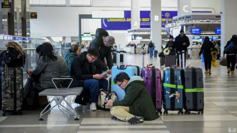 Bloomberg via Getty Images Travelers sit and crouch near a row of large suitcases inside a modern airport terminal