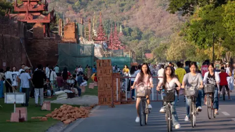 Jonathan Head/ BBC Young women cycling on a road past the royal palace in Mandalay. 