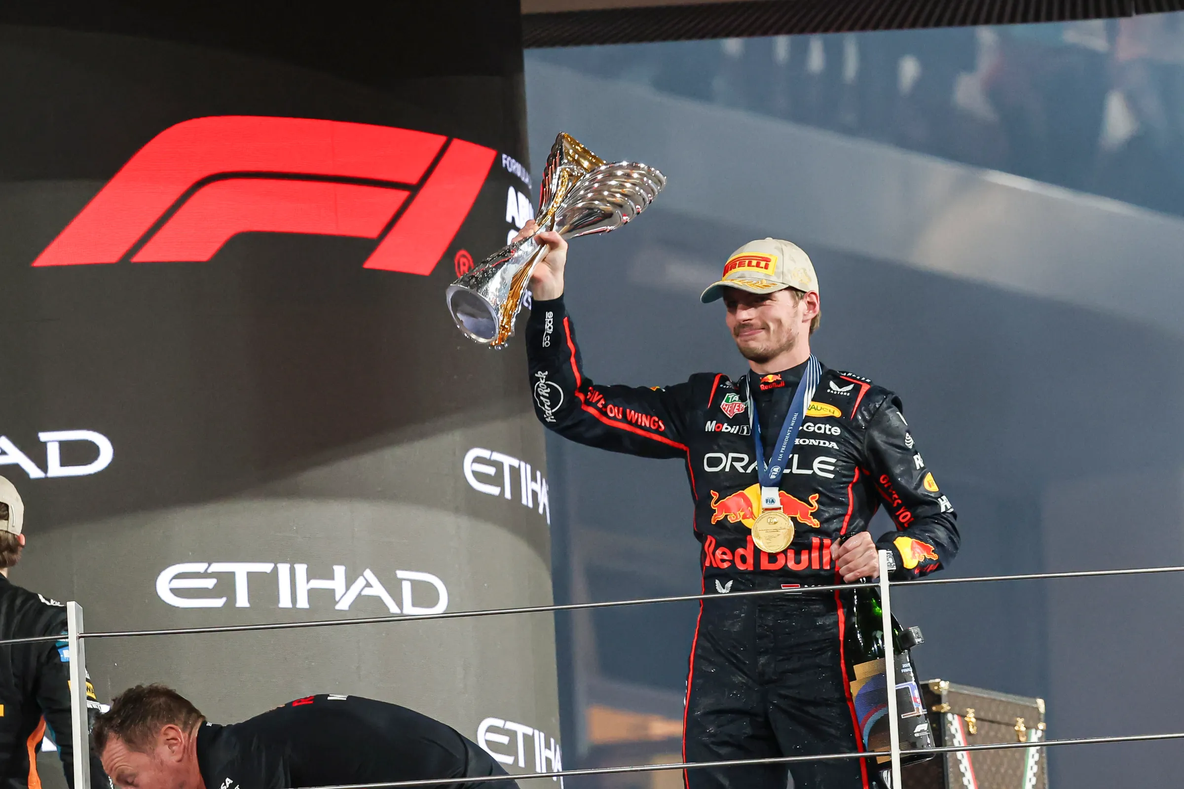 A man holds a trophy and has a medal around his neck, with Redbull costuming for an F1 race