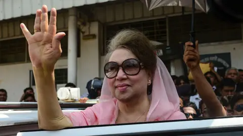 Getty Images Khaleda Zia, in pink, waves as she leaves after a court appearance in Dhaka in 2016