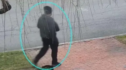 FBI A person dressed head to toe in black is seen walking along a pavement, with a blue ring drawn around them.