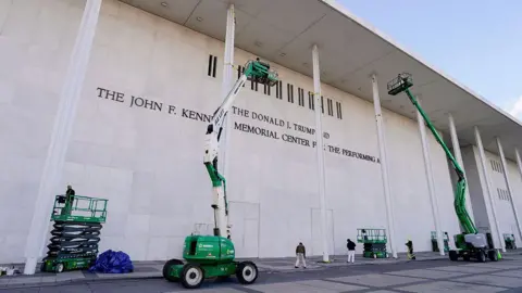 Bloomberg via Getty Images Workers outside the Kennedy Center are on lifts in front of the building, where a sign now says "The Donald J. Trump and The John F. Kennedy Memorial Center for the Performing Arts" 