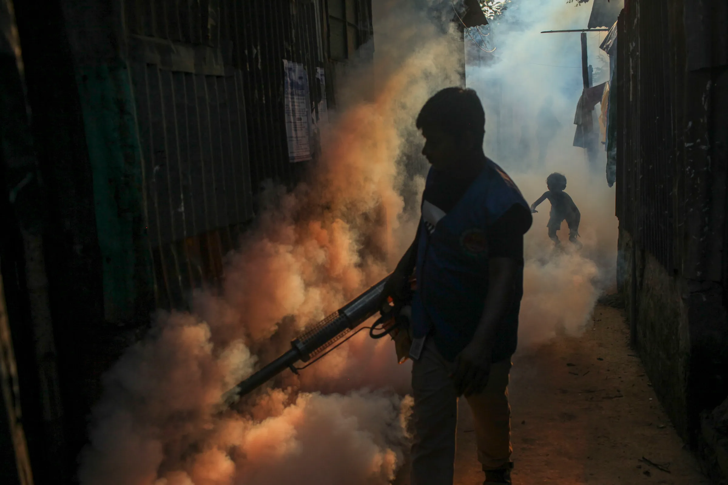 A worker fumigates an alleyway in a densely populated neighborhood to kill mosquitoes