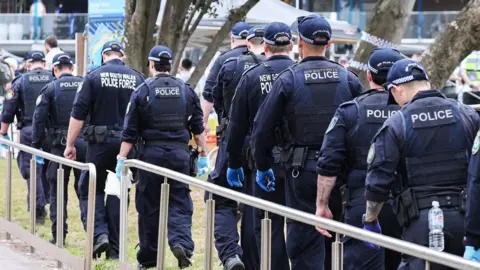 AFP via Getty Images A line of police officers in uniform walk along a fence by Bondi Beach on 16 December.