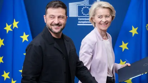 Thierry Monasse/Getty Images President of Ukraine Volodymyr Zelenskyy (L) and the EU Commission President Ursula von der Leyen (R) walk in front of blue and yellow-starred European Union flags