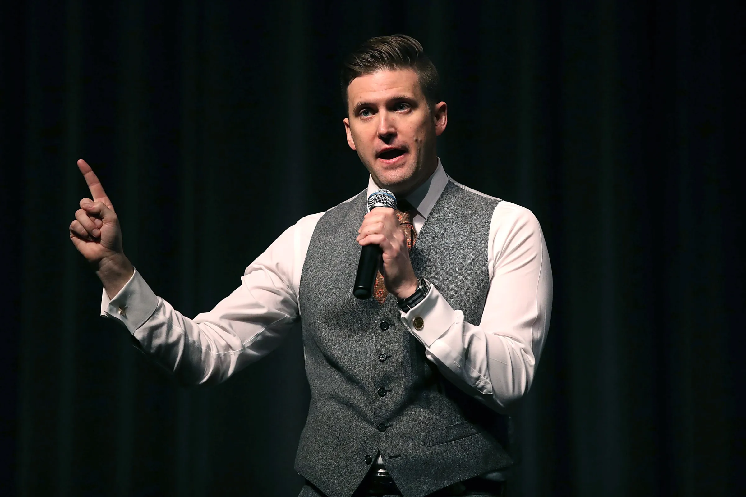 Richard Spencer, in a vest and tie, speaks into a microphone.