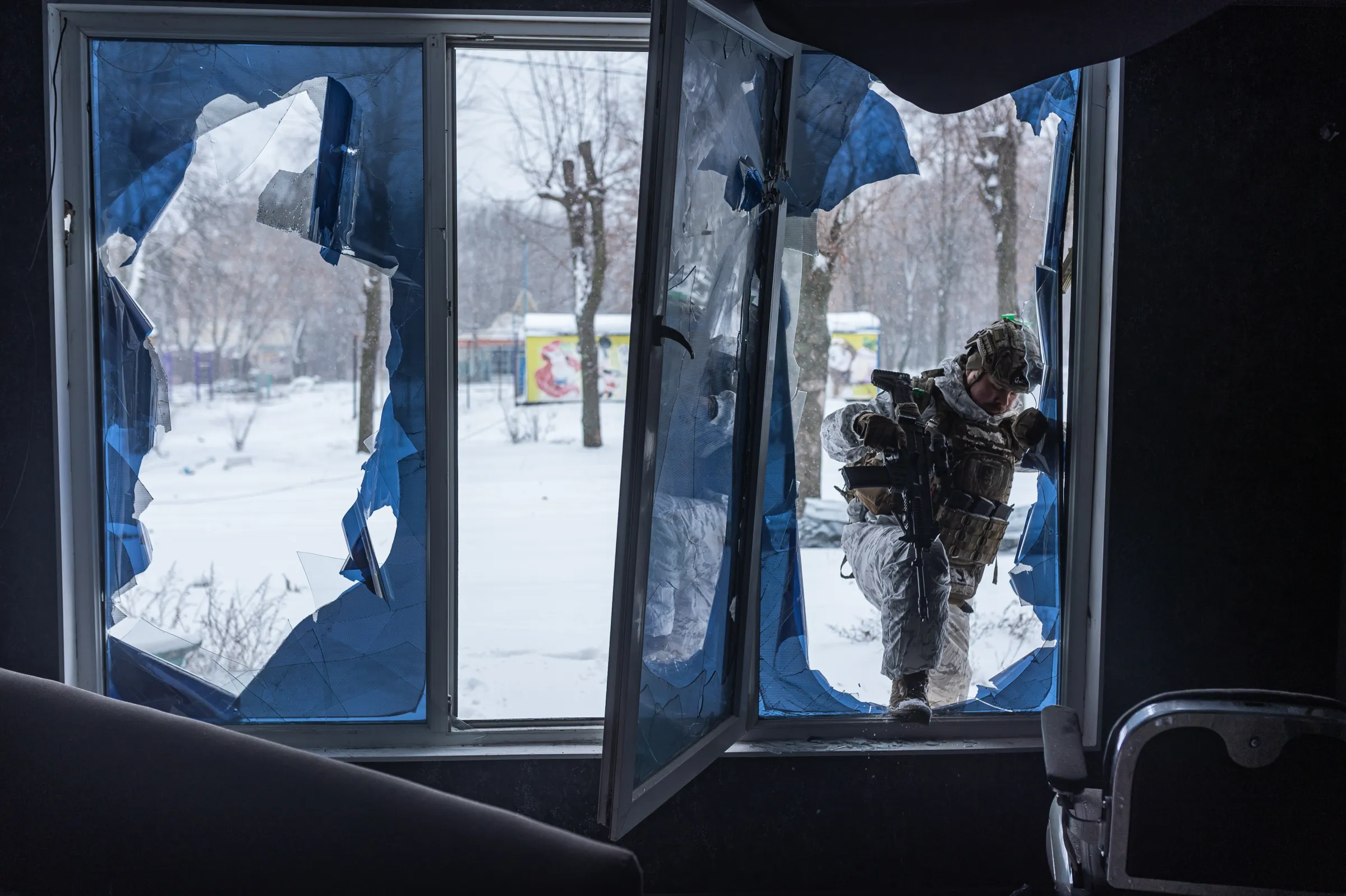 A service member enters a building where a window has been destroyed.
