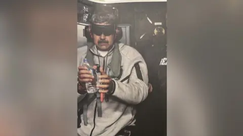 Donald Trump Nicolás Maduro shown after his arrest, wearing headphones and a blindfold, grey zipped jumper