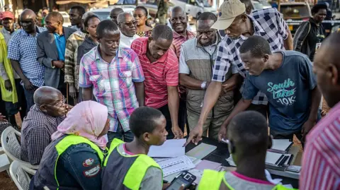 AFP via Getty Images Voters gather around a desk speaking with electoral officials in Kampala 