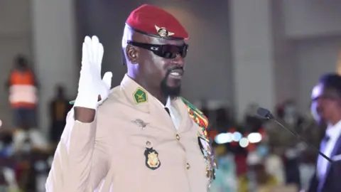AFP via Getty Images Doumbouya in formal military uniform and red beret holds up a white gloved hand to be sworn in in 2021.