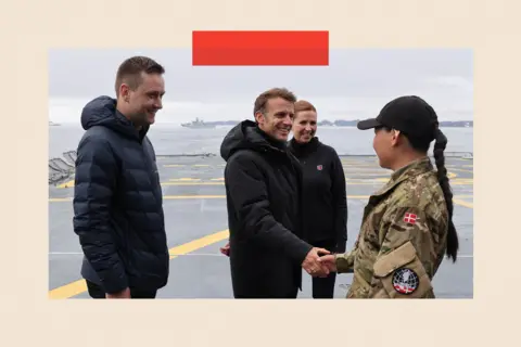 AFP via Getty Images French President Emmanuel Macron (2L) shakes hands with a military personnel flanked by Prime Minister of Greenland Jens-Frederik Nielsen (L) and Denmark's Prime Minister Mette Frederiksen (R)
