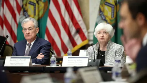 Getty Images A man and a women wearing suits sit in front of microphones.
