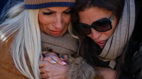 Reuters Women hold hands at a makeshift memorial outside the Le Constellation bar