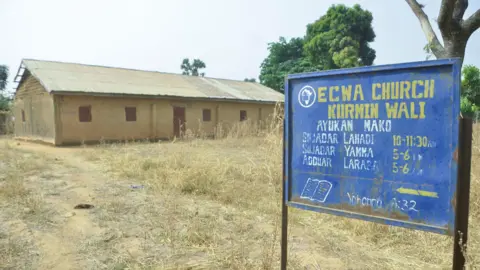 Reuters Exterior view of ECWA Church, after an attack by gunmen in which worshippers were kidnapped.  The church is made of brown bricks.  There is a blue sign with the name of the church and service times in yellow.   