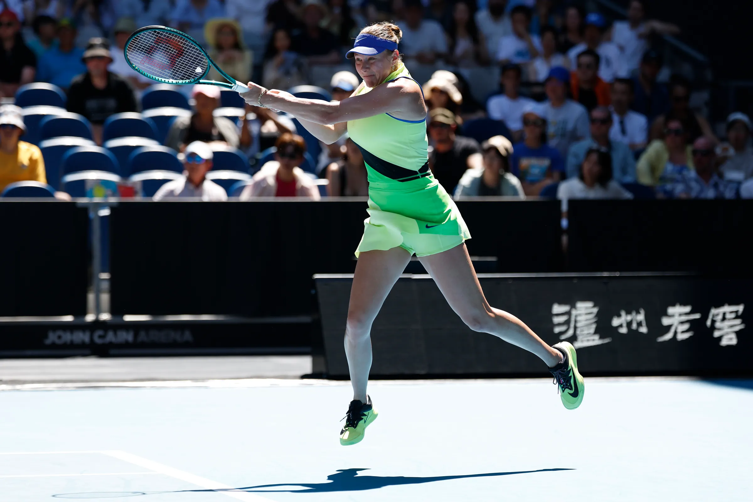 Amanda Anisimova, in a light green tennis outfit, shown after a powerful swing on the tennis court.